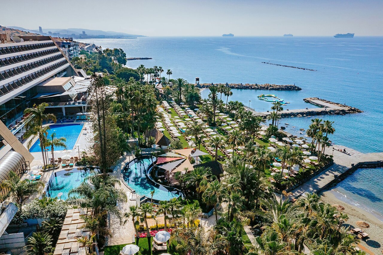 Amathus Beach Hotel Limasolā, Kiprā — panorāmas skats uz baseiniem, tropu dārzu un Vidusjūras piekrasti saulainā dienā