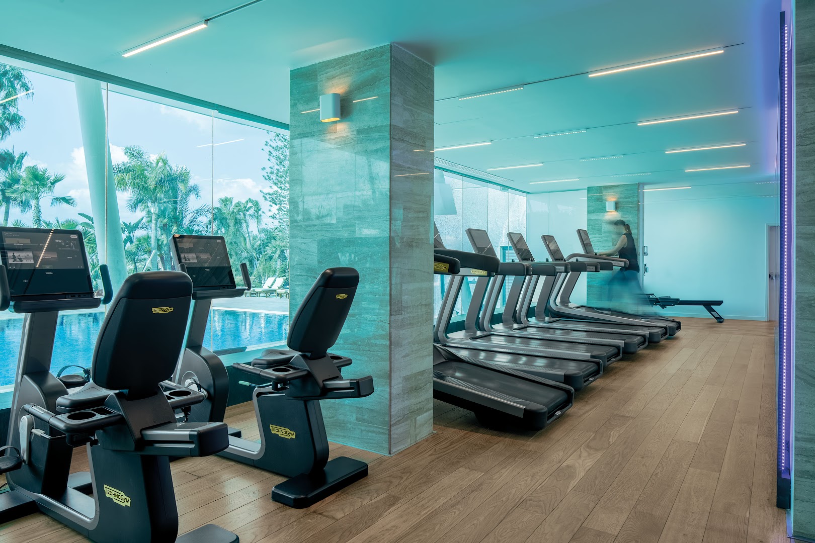 Amathus Beach mūsdienīgs fitness centrs ar skrejceliņiem un skatu uz āra baseinu caur stiklotu sienu Limasolā