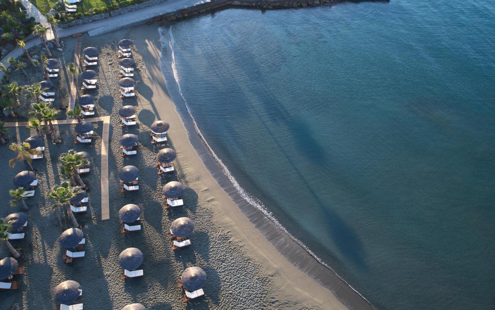 Amathus Beach Hotel pludmales skats no augšas — sakārtotas saulessargu rindas un sauļošanās krēsli pie dzidra jūras ūdens