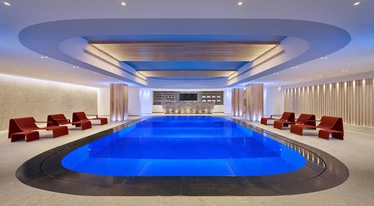 Parklane Resort & Spa iekštelpu baseins ar zilu apgaismojumu un sarkaniem dizaina atpūtas krēsliem spa centrā Limasolā