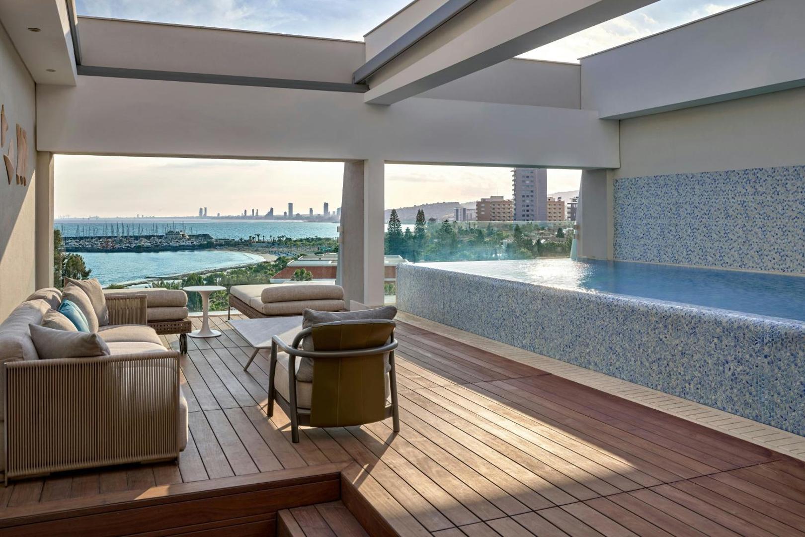 Parklane Resort & Spa jumta terase ar atpūtas mēbelēm un baseinu, fonā Limasolas pilsētas panorāma un jahtu piestātne