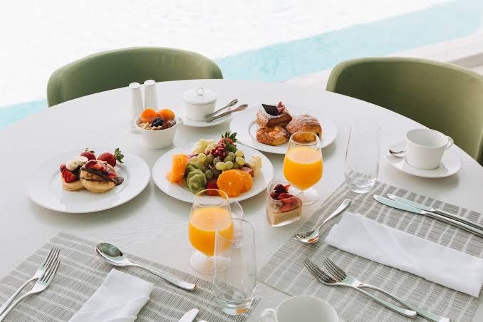 Brokastu galds Parklane Resort & Spa ar svaigiem augļiem, smalkmaizītēm un sulu — eleganta maltīte pie baseina