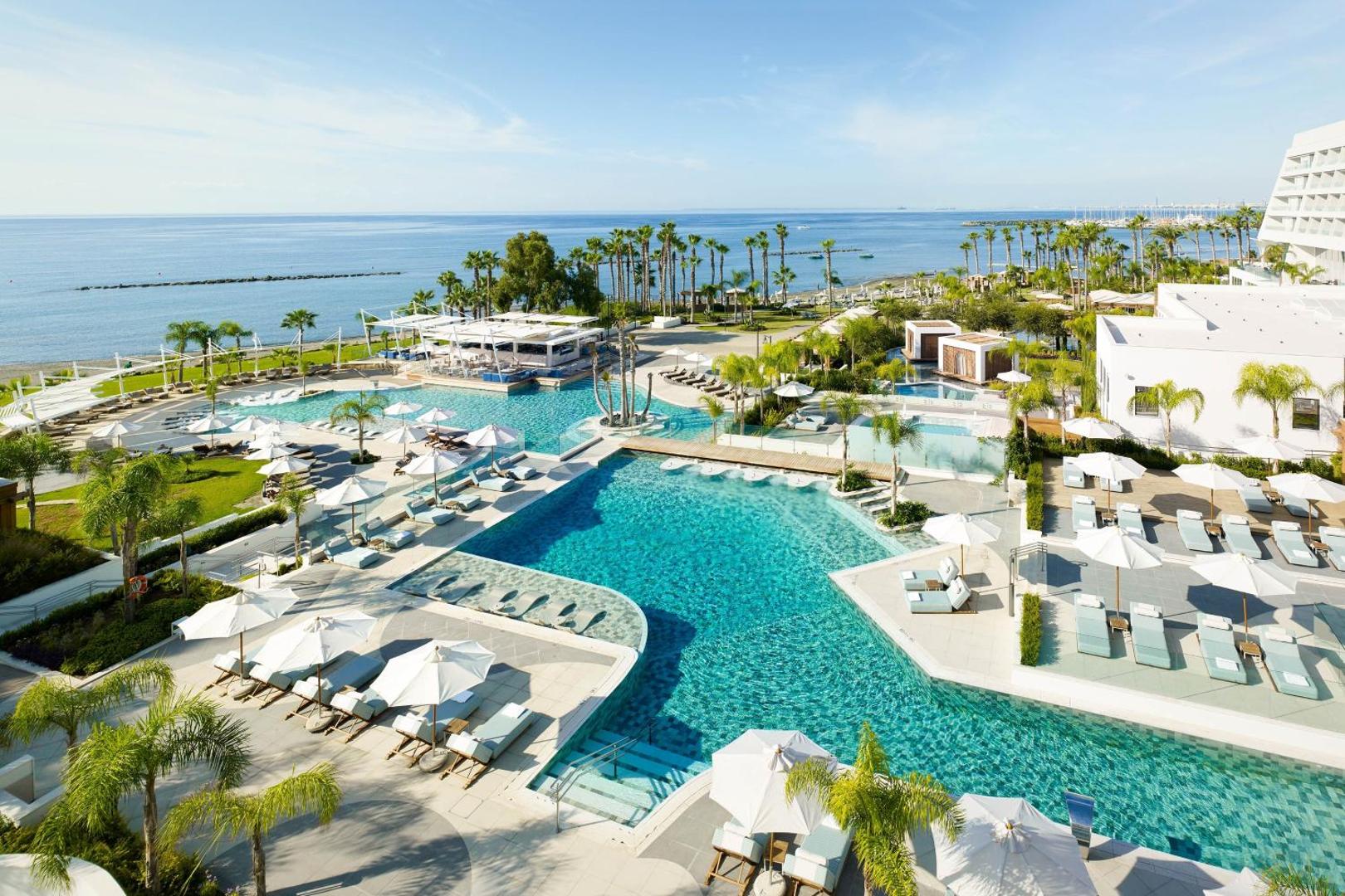 Parklane Resort & Spa plašais āra baseinu komplekss ar palmām, saulessargiem un skatu uz jūru Limasolā, Kiprā