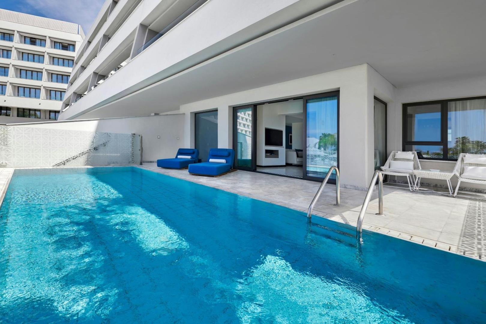 Parklane Resort & Spa numurs ar tiešu piekļuvi baseinam Limasolā, Kiprā — privāta terase ar ziliem sauļošanās krēsliem un modernu dizainu