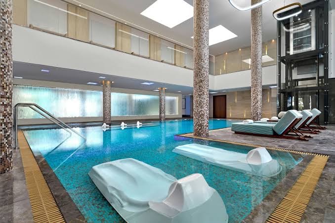Luksusa spa baseins viesnīcā Parklane Resort & Spa ar masāžas gultām ūdenī, mozaīkas kolonnām un modernu apgaismojumu