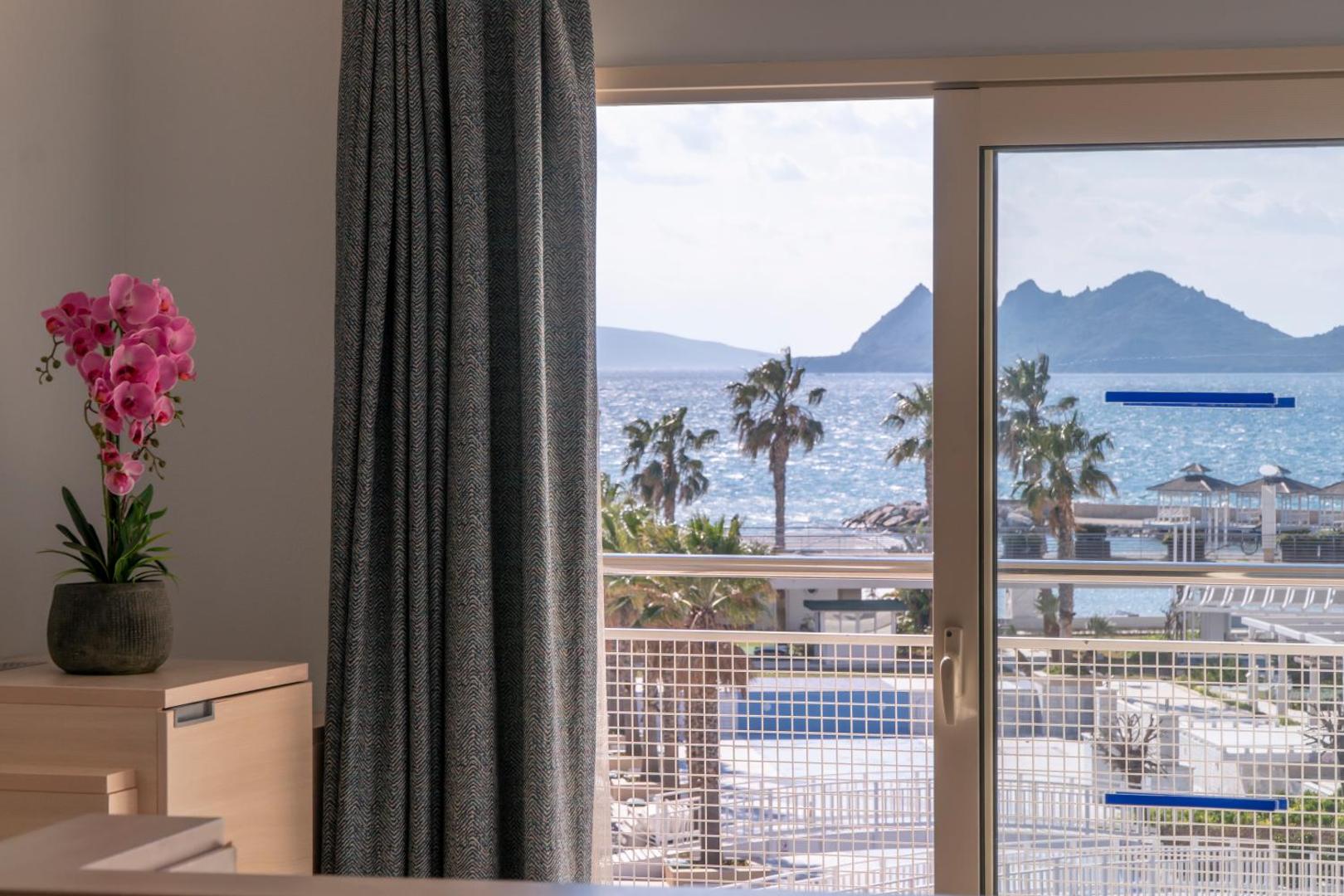 Skats caur La Blanche Resort & Spa numura logu uz Egejas jūru, palmām un kalniem Bodrumas piekrastē