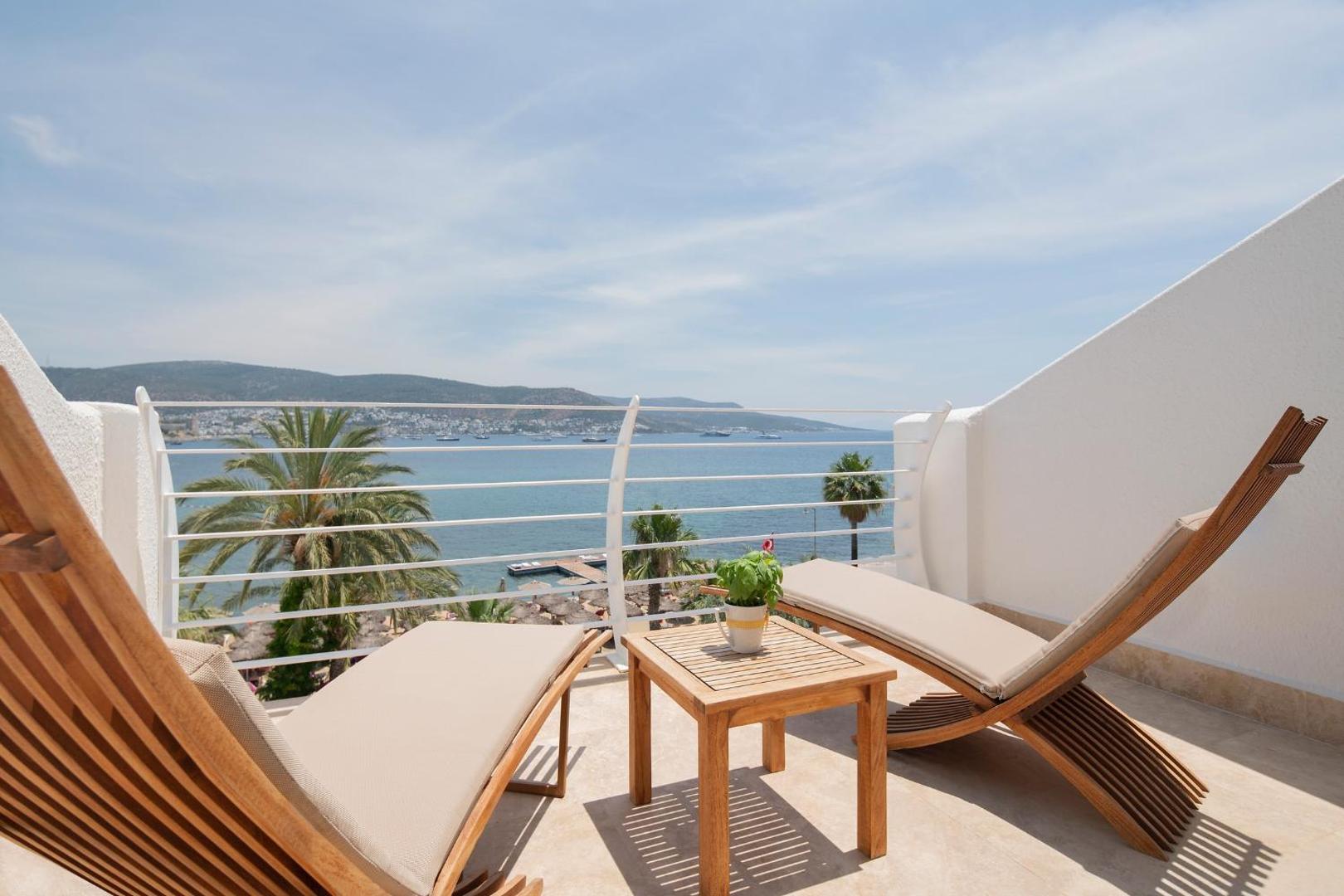 Prive Hotel Bodrum privātais balkons ar koka atpūtas krēsliem un galdiņu, skats uz palmu dārzu un jūru