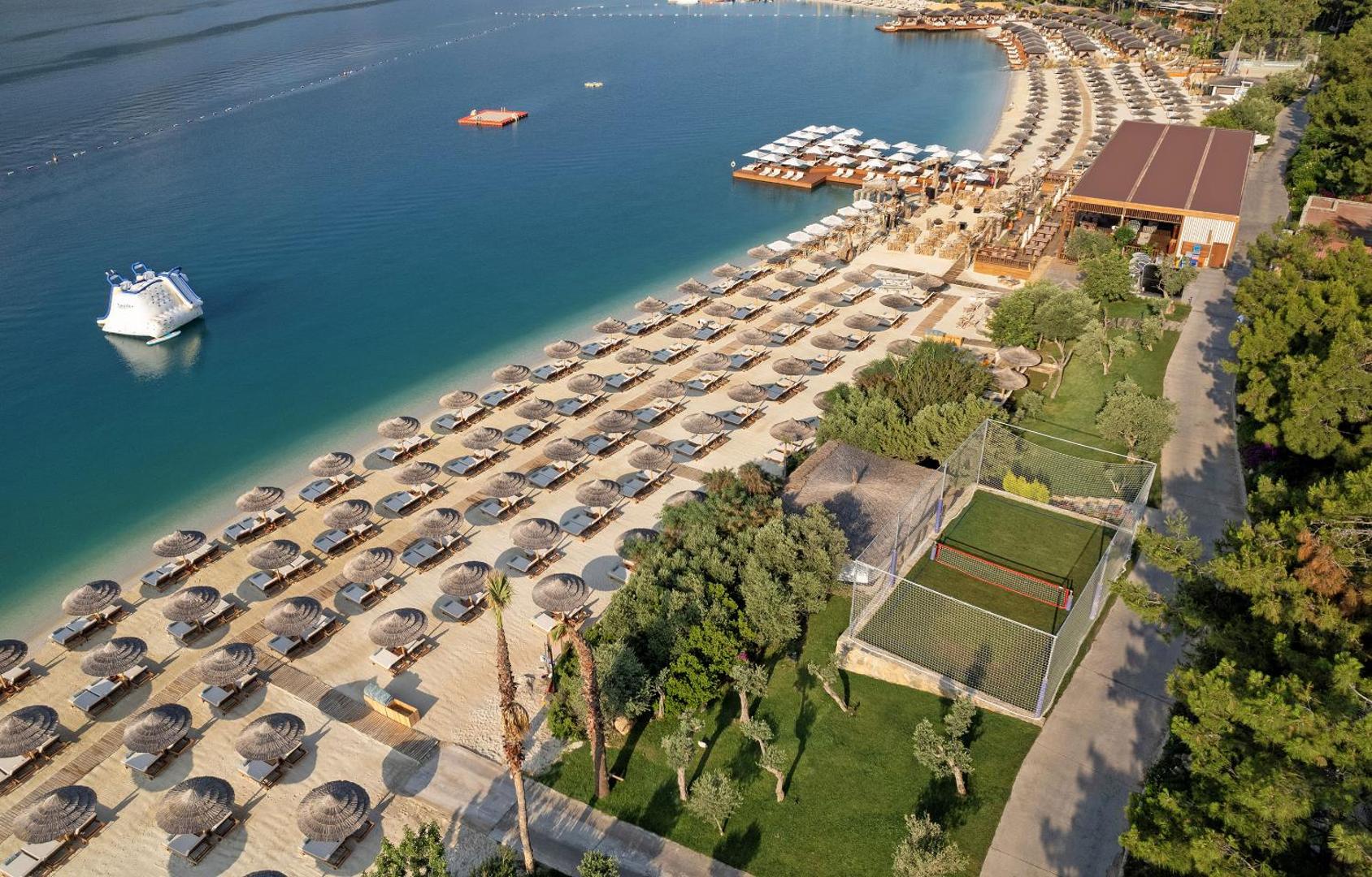 Titanic Luxury Collection Bodrum kūrorta panorāma ar plašu pludmali, sporta laukumu, saulessargiem un ūdens atrakcijām Egejas jūras krastā