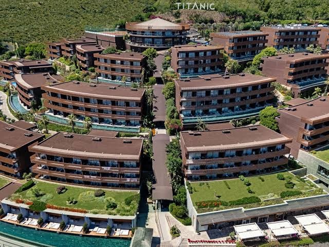 Titanic Luxury Collection Bodrum numuru korpusi ar zaļajiem jumtiem un terasēm, izvietoti kaskādes veidā Bodrumas piekrastes kalnā
