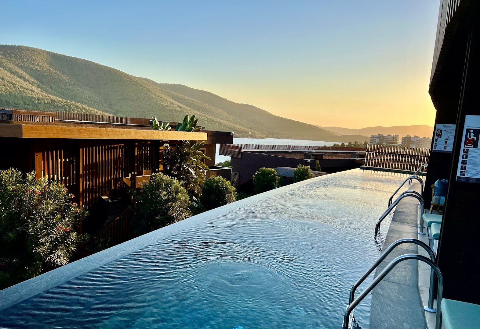 Titanic Luxury Collection Bodrum bezgalības baseins saulrieta laikā ar skatu uz kalnaino piekrasti un kūrorta arhitektūru