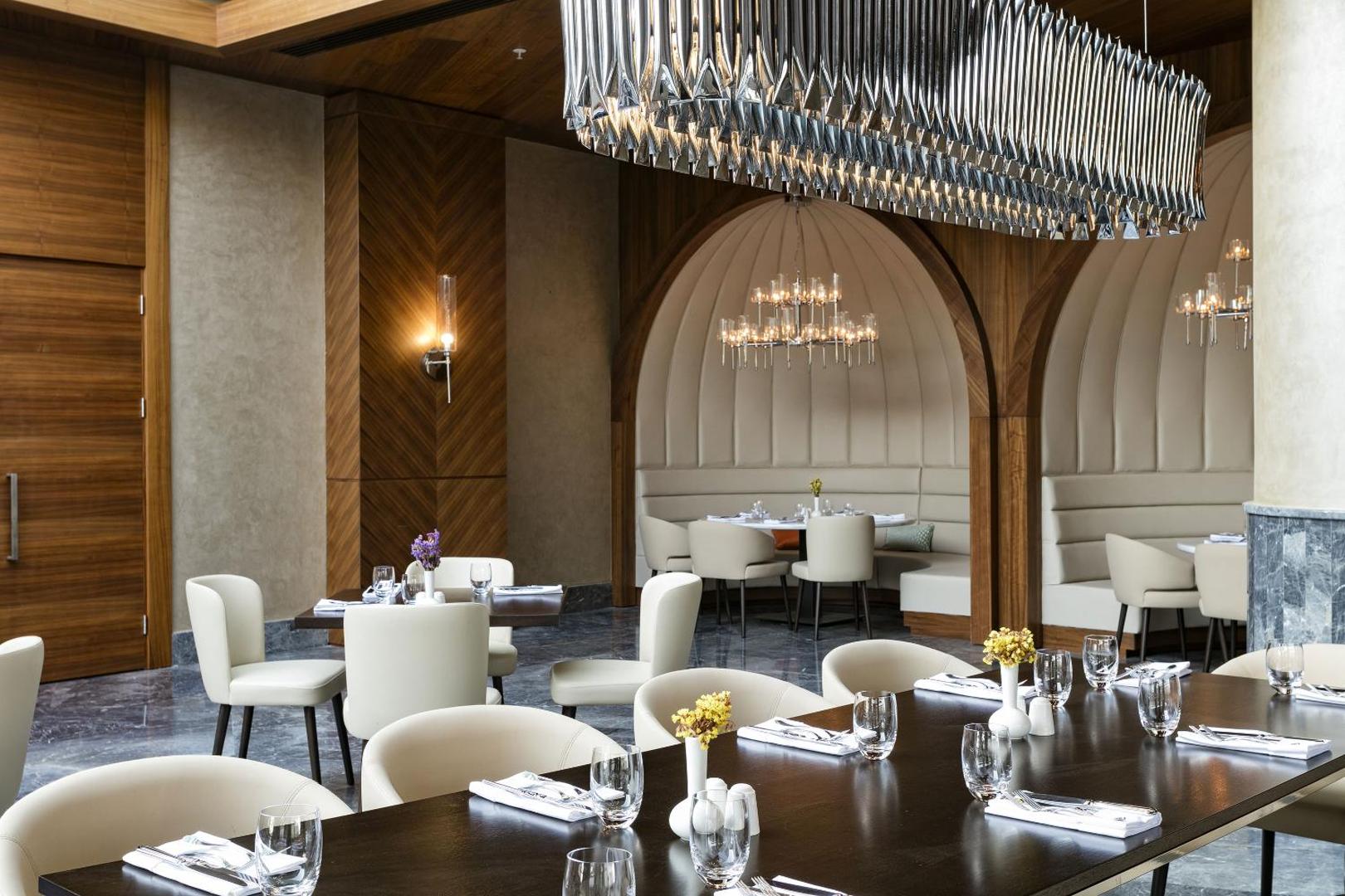 Elegants Titanic Luxury Collection Bodrum restorāna interjers ar dizaina lustrām, apaļiem galdiem un mīkstajiem dīvāniem nišās