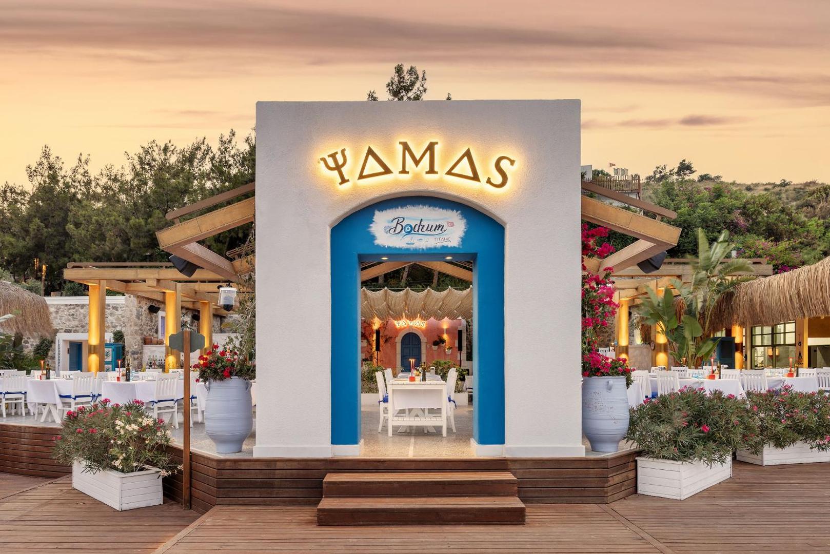 Grieķu stila restorāns Yamas viesnīcā Titanic Luxury Collection Bodrum ar baltiem galdiem un ziliem akcentiem āra terasē