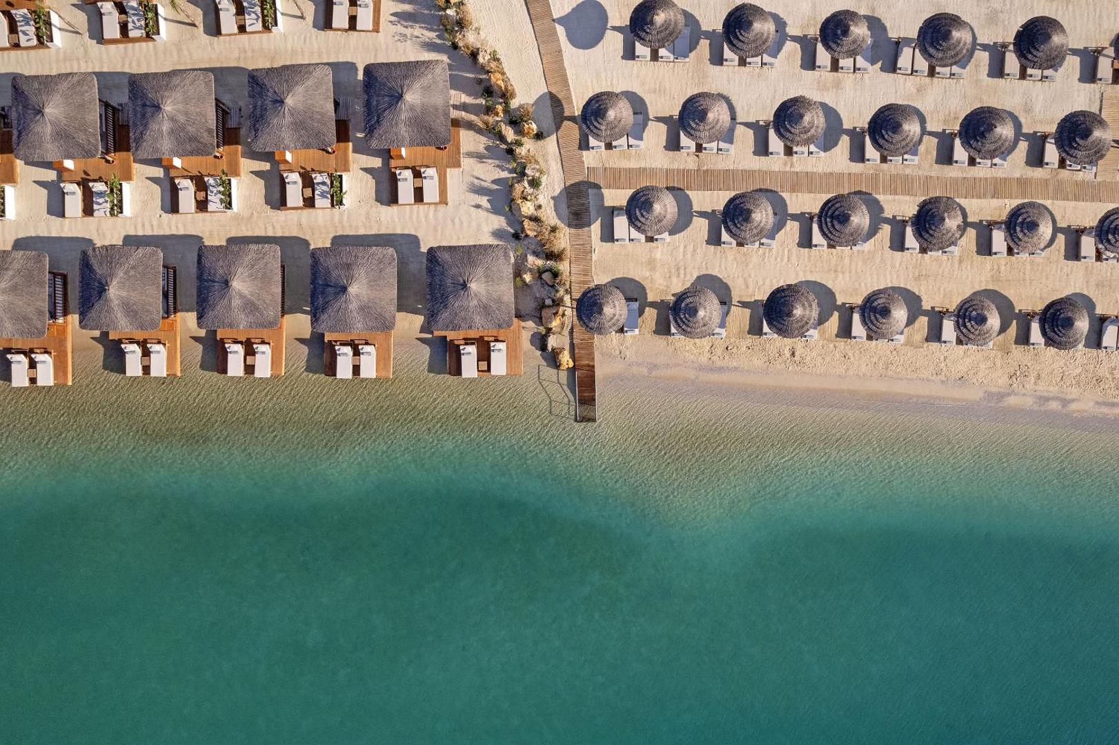 Aerofoto skats uz Titanic Luxury Collection Bodrum privāto pludmali ar salmu saulessargiem, zviļņiem un dzidru, tirkīzzilu jūras ūdeni