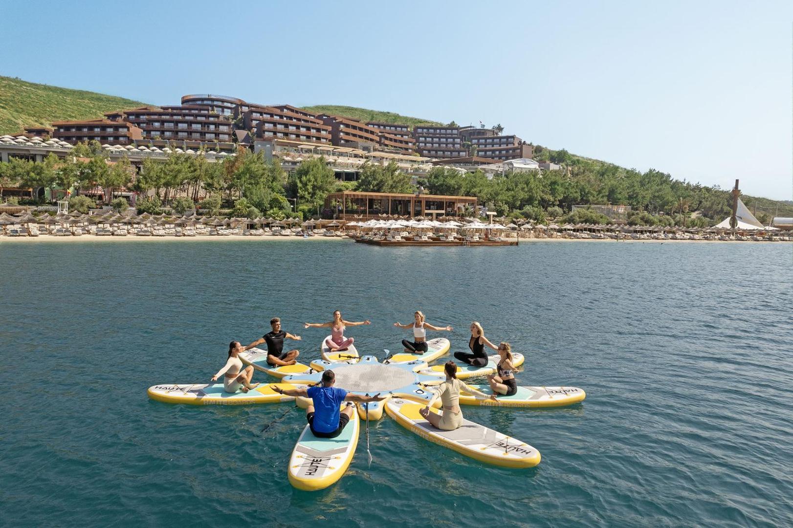 Titanic Luxury Collection Bodrum viesnīcas ēka piekrastē un jogas nodarbība uz SUP dēļiem jūrā