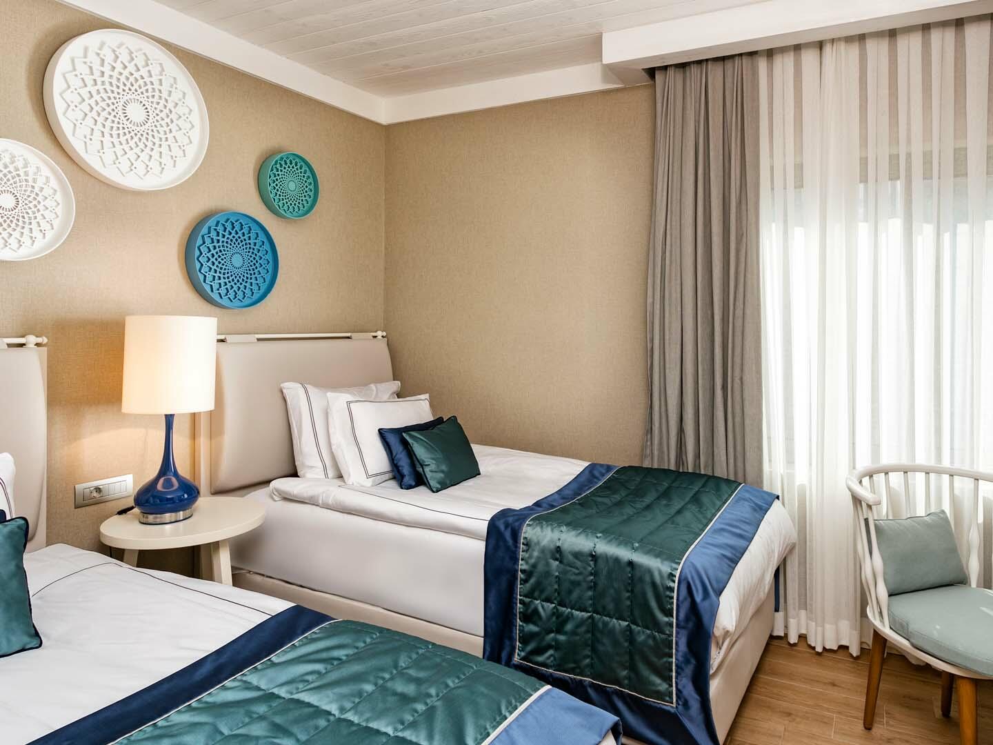 Gaišs Titanic Luxury Collection Bodrum viesnīcas numurs ar divām gultām, ziliem akcentiem un dekoratīviem elementiem pie sienas