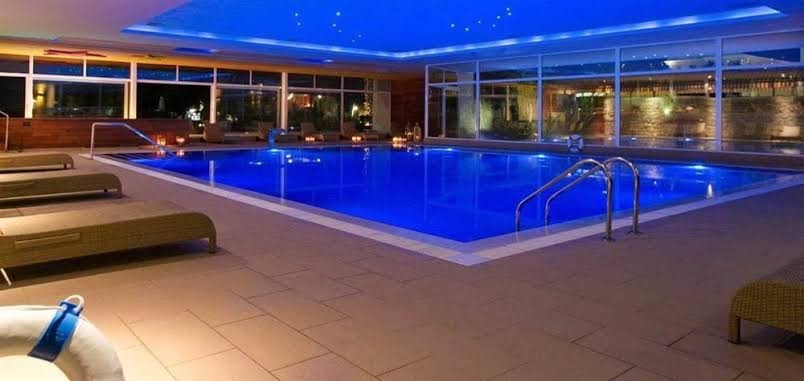 Palas viesnīcas spa centra iekštelpu baseins ar zilu nakts apgaismojumu un ērtiem zviļņiem — romantiska vakara atpūta