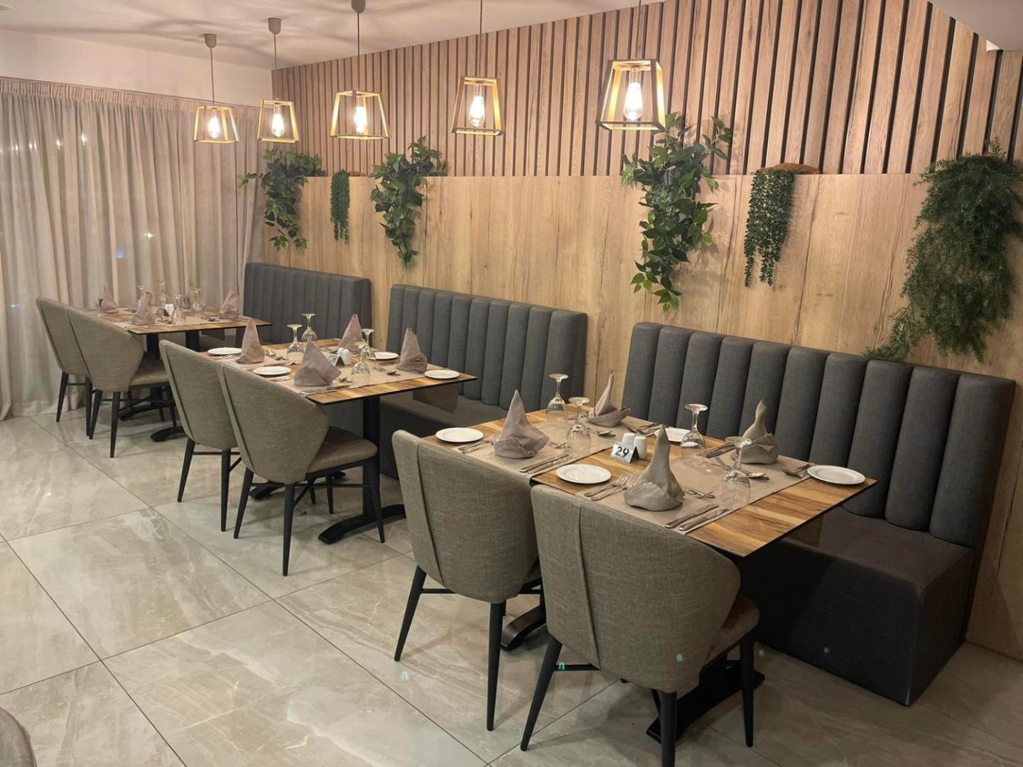 Bohemian Gardens Hotel restorāna zona ar mīkstajiem dīvāniem un koka sienas paneļiem — elegants apgaismojums un dekoratīvie augi