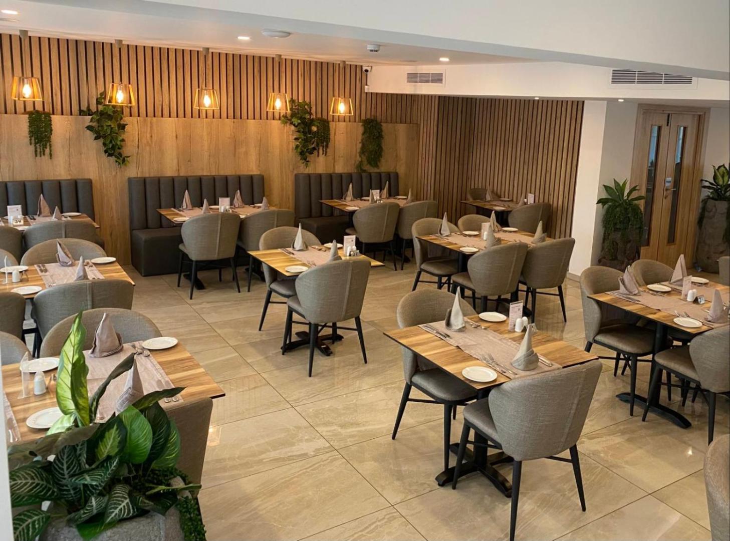 Bohemian Gardens Hotel restorāna zāle Protarasā, Kiprā — moderns interjers ar koka elementiem, pelēkiem krēsliem un eleganti klātiem galdiem