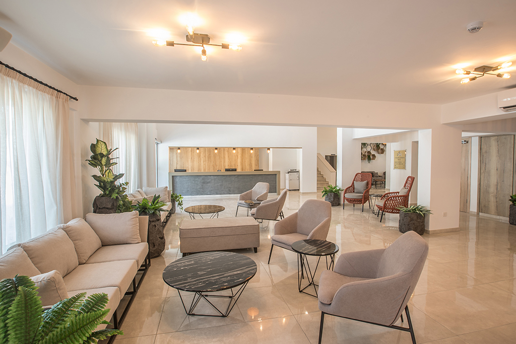 Bohemian Gardens Hotel gaišā lobby zona Protarasā — plaša atpūtas telpa ar moderniem dīvāniem, atpūtas krēsliem un recepcijas galdu