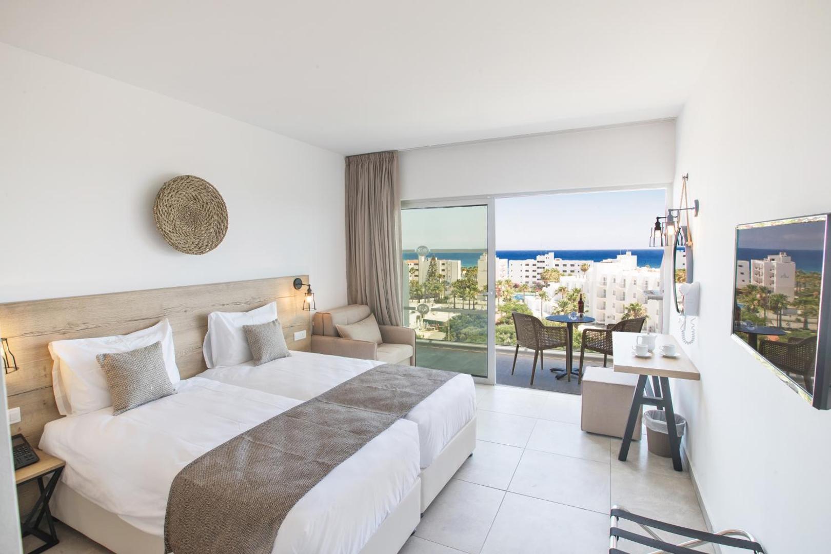 Bohemian Gardens Hotel gaišs divvietīgs numurs ar panorāmas logu uz balkonu, no kura paveras skats uz kūrortu un jūru