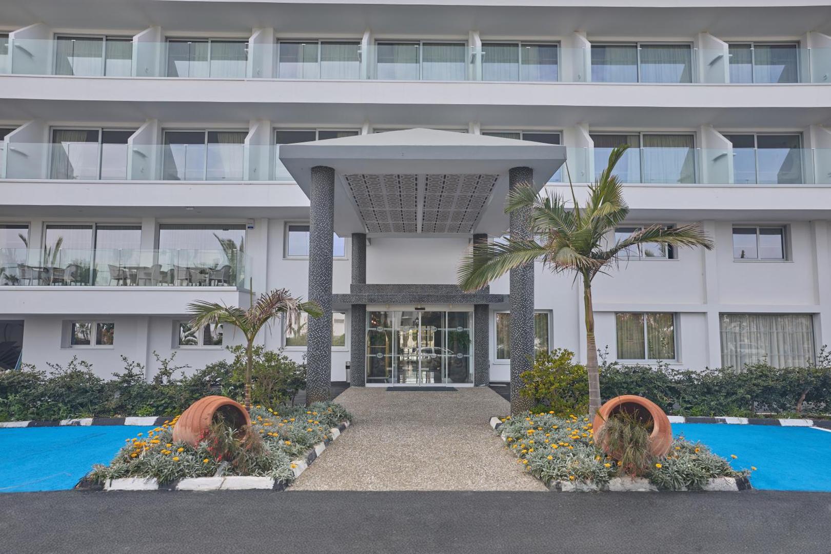 Bohemian Gardens Hotel galvenā ieeja ar modernu nojumi, dekoratīviem māla traukiem un ziedu dobēm Protarasā