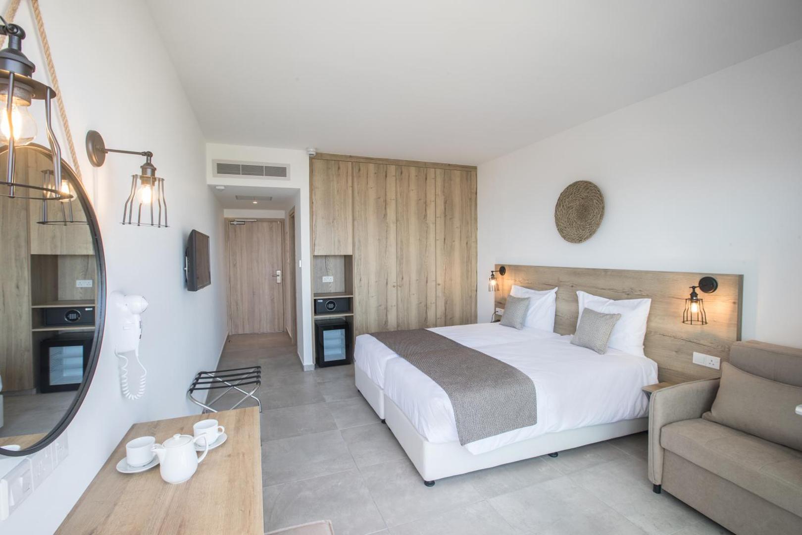 Bohemian Gardens Hotel moderns numura interjers ar koka elementiem, lielu gultu, atpūtas krēslu un darba zonu