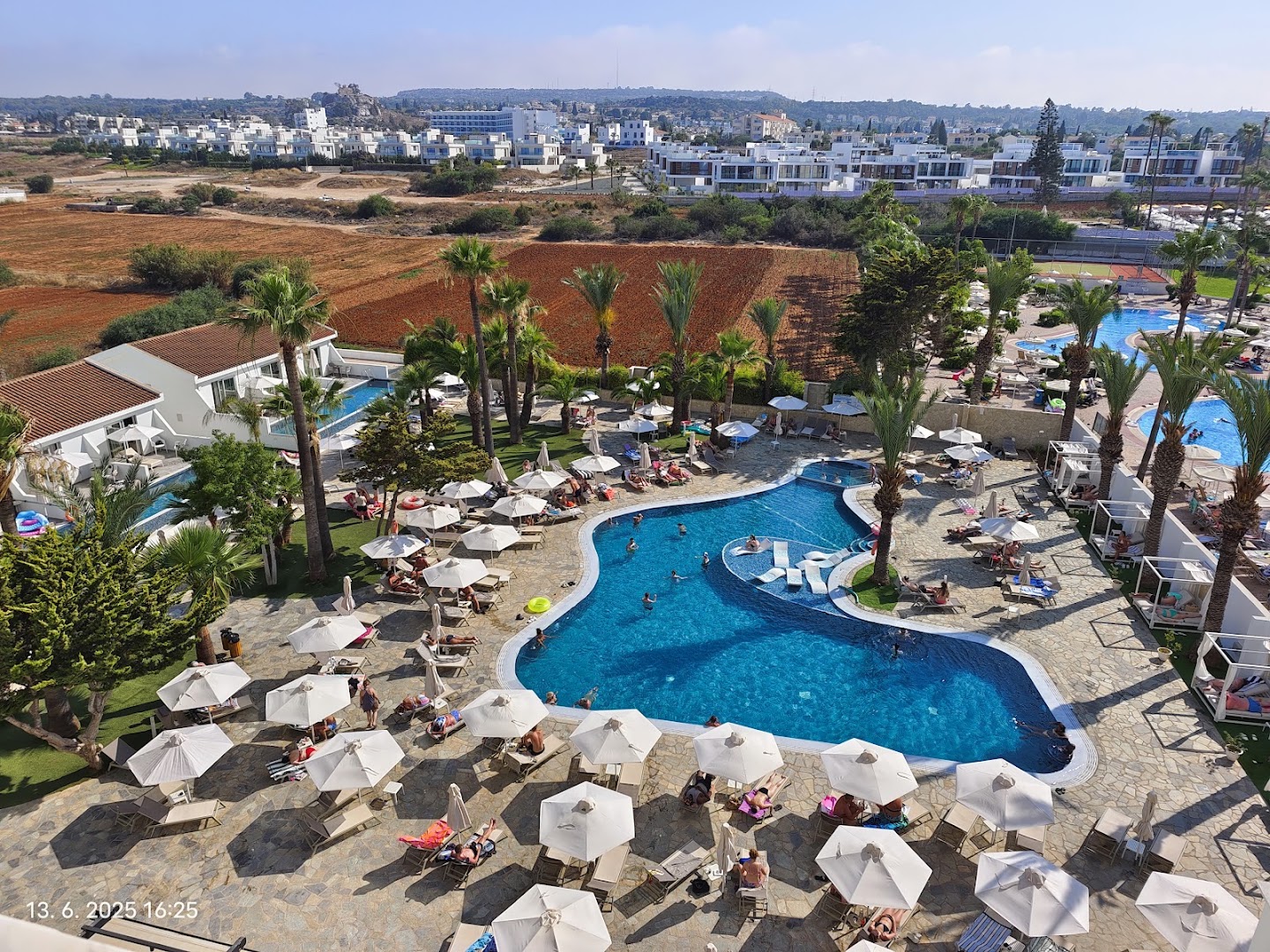 Bohemian Gardens Hotel galvenais baseins ar atpūtas zonu, saulessargiem un palmām Protaras kūrortā Kiprā no augšas