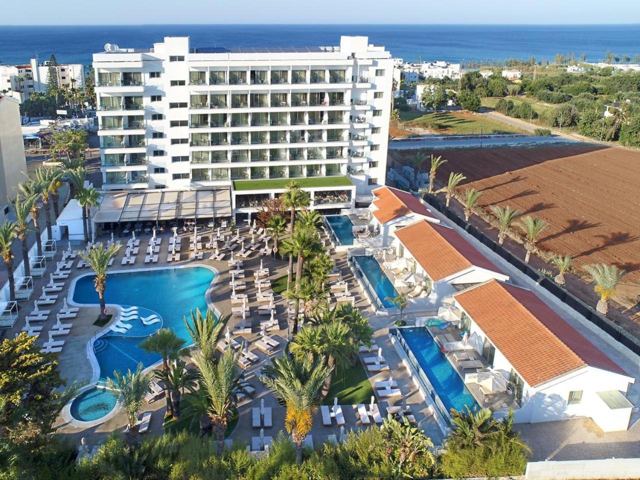 Bohemian Gardens Hotel kopskats no putna lidojuma Protarasā, Kiprā — galvenā ēka, vairāki āra baseini, sauļošanās terases un palmas piekrastē