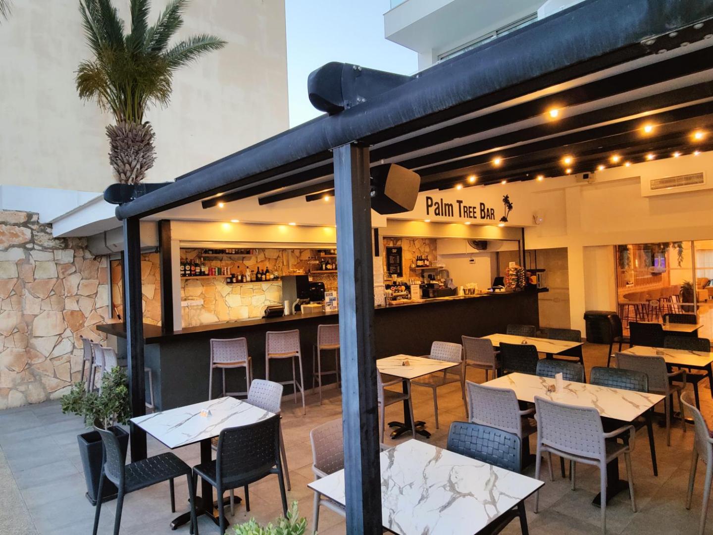 Bohemian Gardens Hotel bārs Palm Tree Bar ar āra galdiņiem un vakara apgaismojumu Protarasas kūrortā