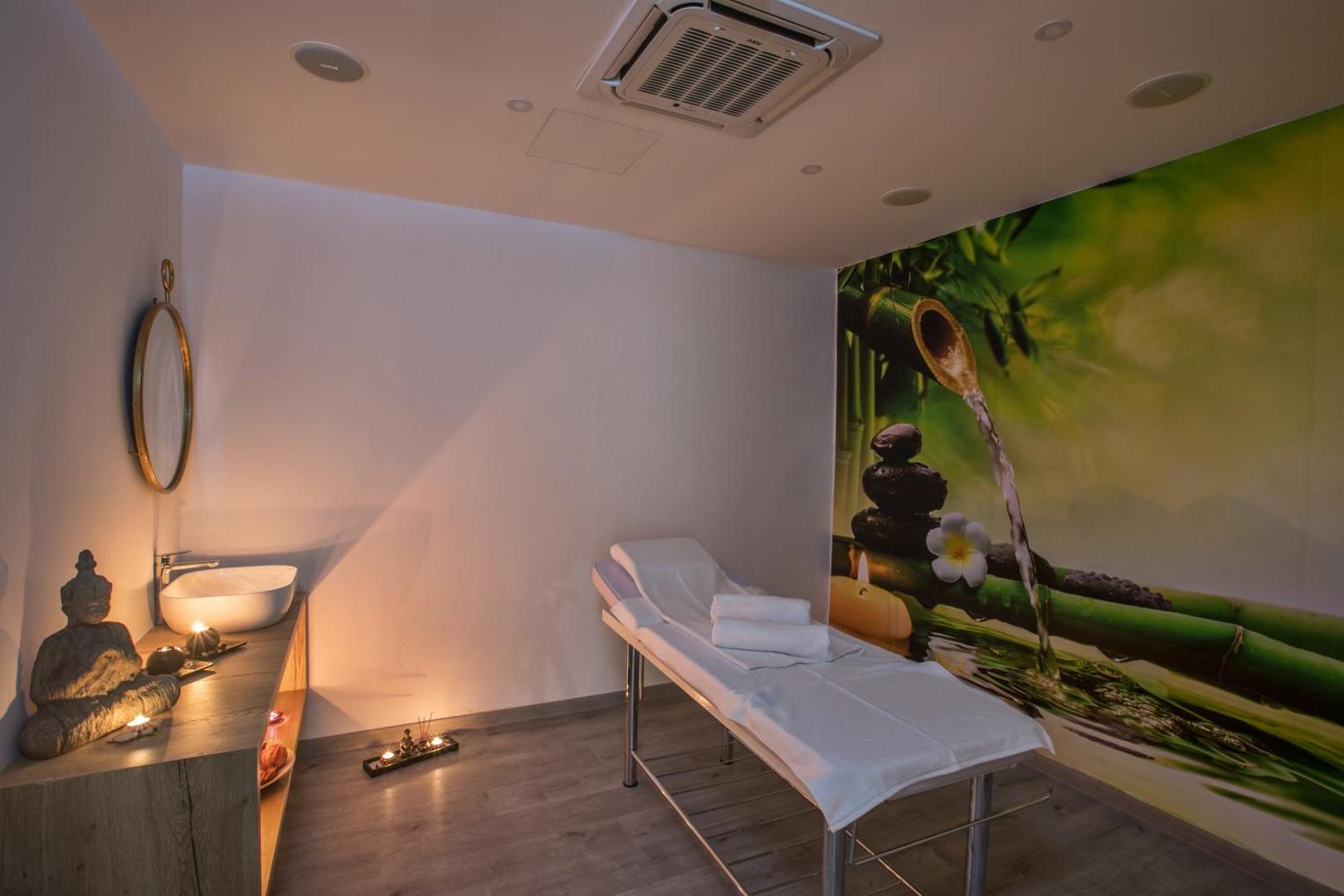 Bohemian Gardens Hotel spa procedūru telpa ar masāžas galdu, dekoratīvu sienas attēlu un mierīgu apgaismojumu relaksācijai