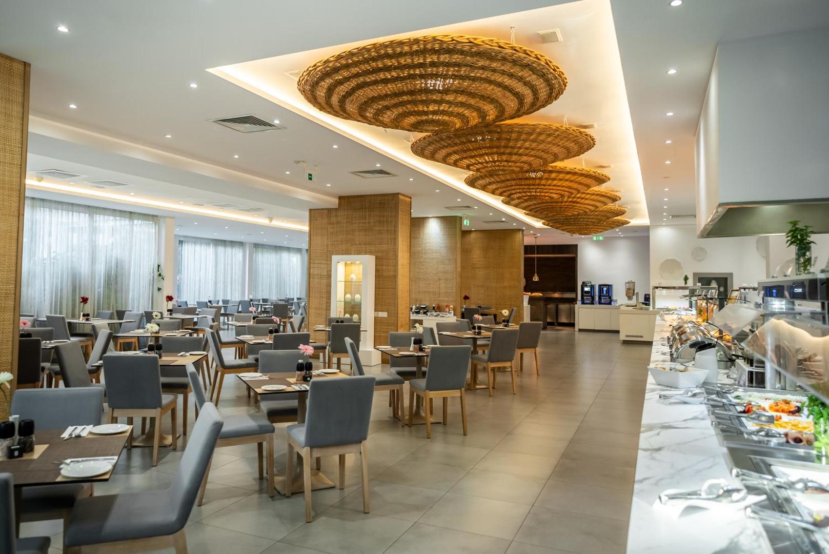 Margadina Lounge viesnīcas galvenais restorāns ar modernām mēbelēm un pītiem griestu dekoriem Aijanapā, Kiprā — plaša bufetes zona un galdiņi