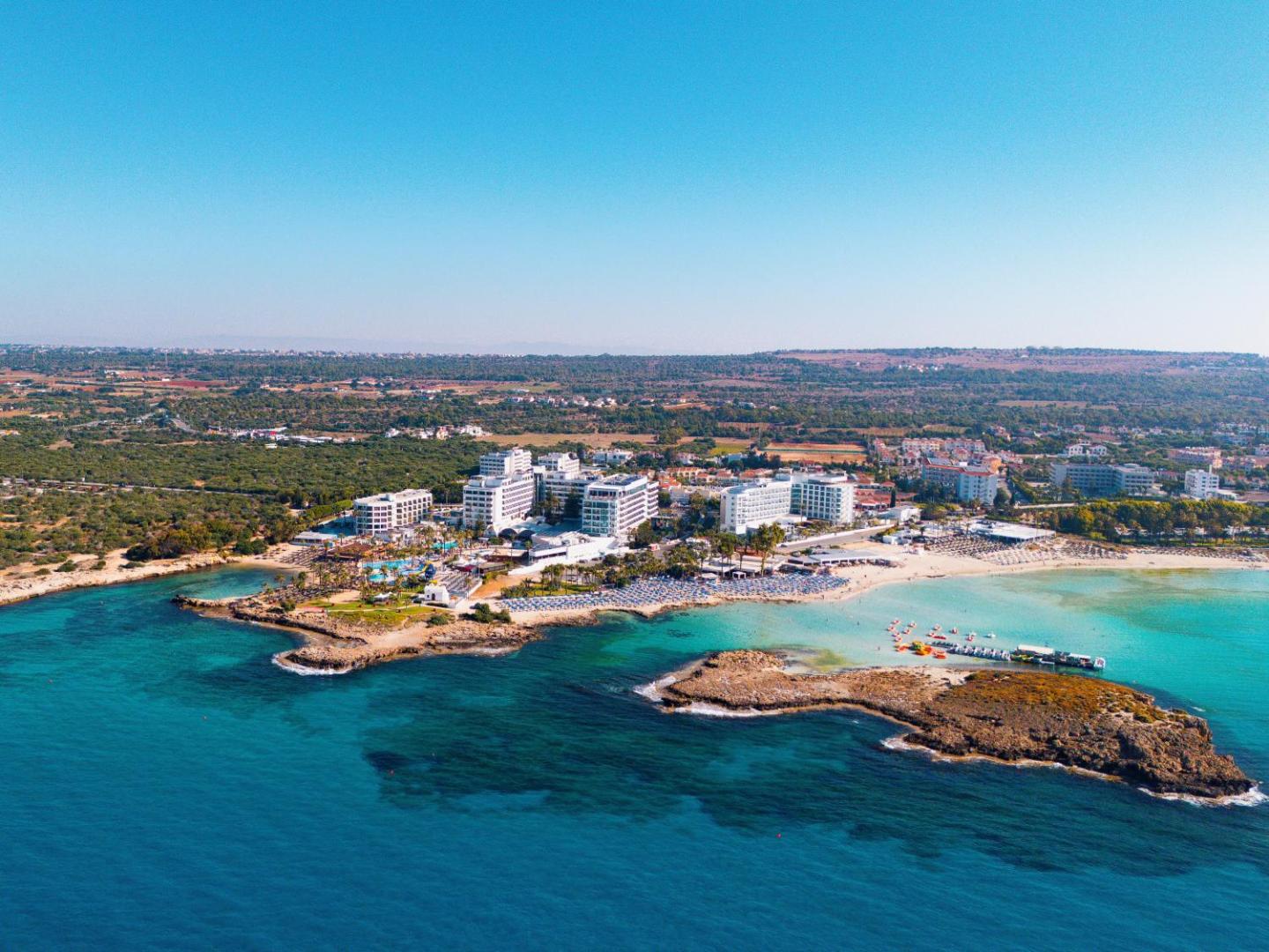 Adams Beach Hotel panorāmas skats no putna lidojuma Ajanapā, Kiprā — viesnīcas komplekss pie tirkīzzila līča un smilšu pludmales