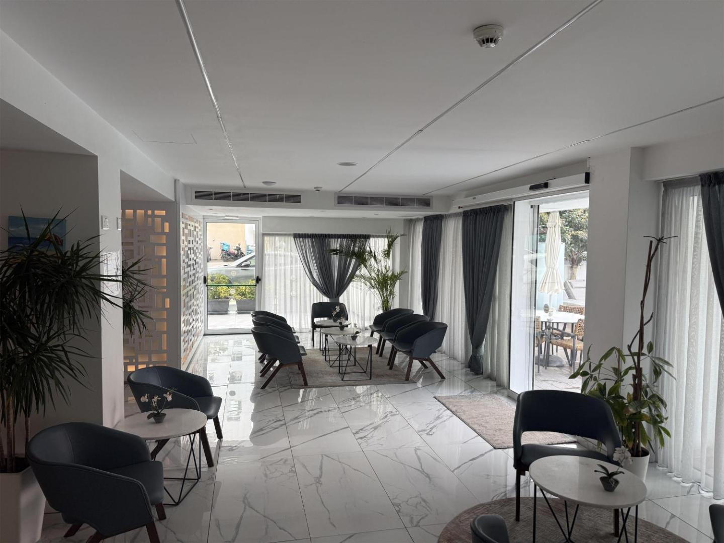 Gaišs Best Western Plus Larco Hotel lobby vestibils ar marmora grīdu, moderniem krēsliem un skatu uz āra terasi Larnakā.