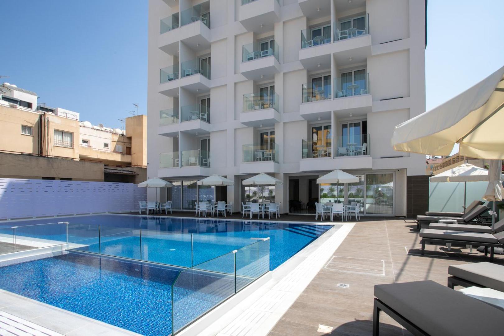 Best Western Plus Larco Hotel modernā fasāde ar balkoniem un āra baseinu, kura malā izvietoti galdiņi un saulessargi.