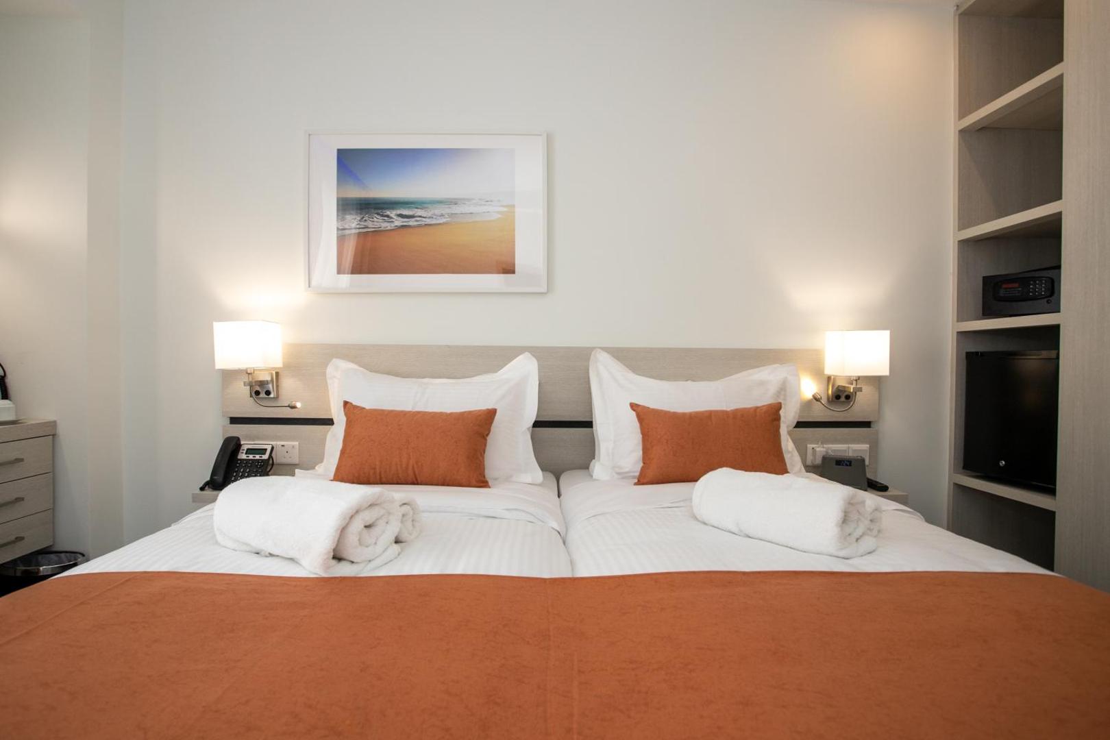 Best Western Plus Larco Hotel gaišs divvietīgs numurs Larnakā ar oranžiem akcentiem, modernām mēbelēm un dekoratīvu gleznu pie sienas.
