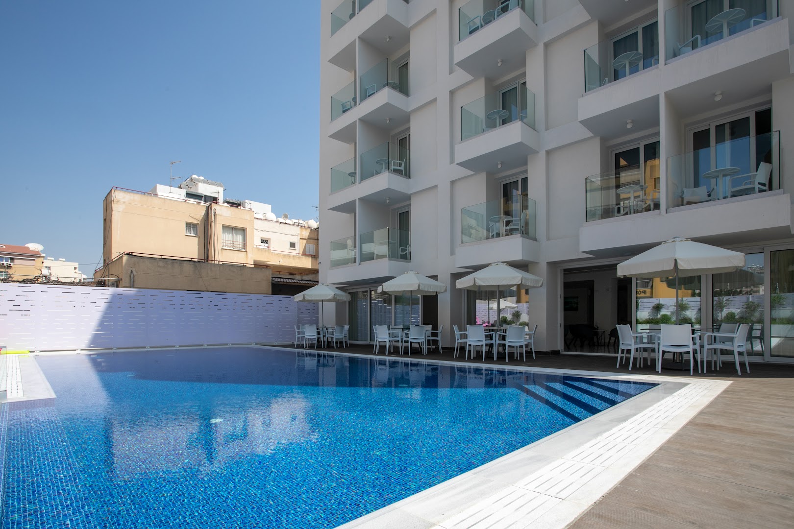 Best Western Plus Larco Hotel dzidri zilais āra baseins Larnakā, blakus viesnīcas ēkai ar stiklotiem balkoniem un atpūtas zonu.