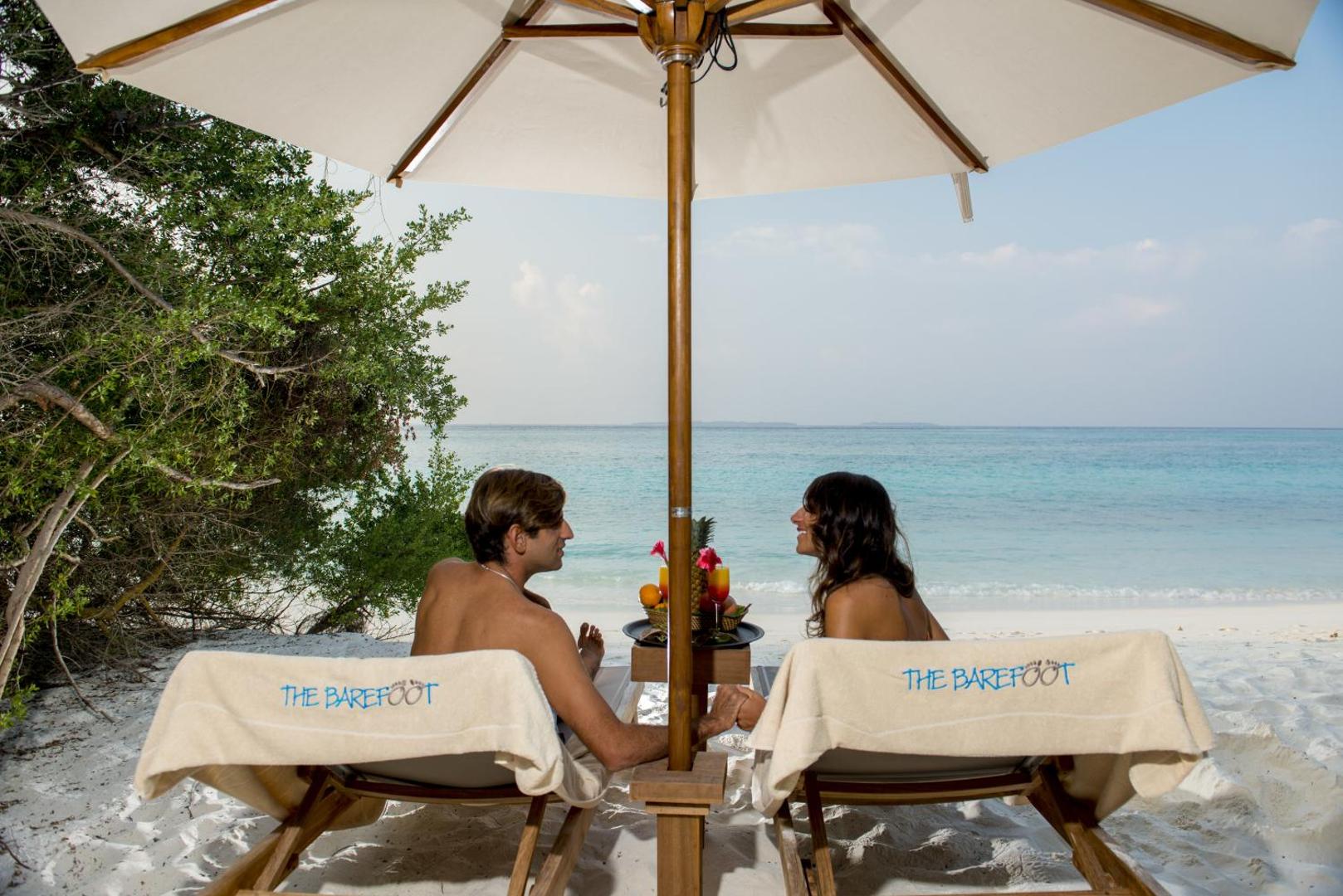 Pāris atpūšas The Barefoot Eco Hotel pludmalē zem saulessarga ar eksotiskiem kokteiļiem un skatu uz tirkīzzilo Indijas okeānu
