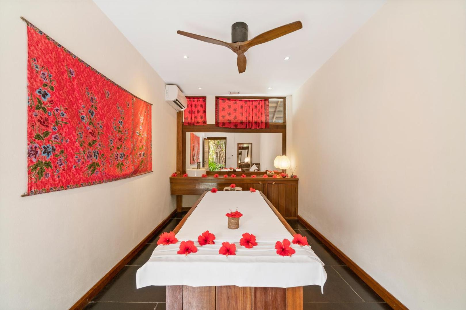 The Barefoot Eco Hotel spa procedūru numurs ar masāžas galdu, dekorēts ar sarkaniem ziediem un tradicionāliem audumiem