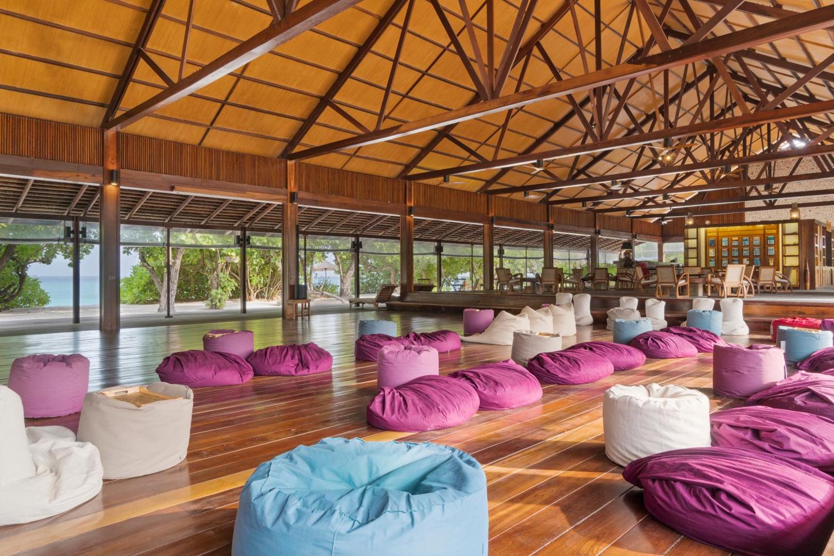 The Barefoot Eco Hotel atpūtas zona ar krāsainiem sēžammaisiem uz koka grīdas plašā, atvērtā tipa paviljonā Maldīvu salās