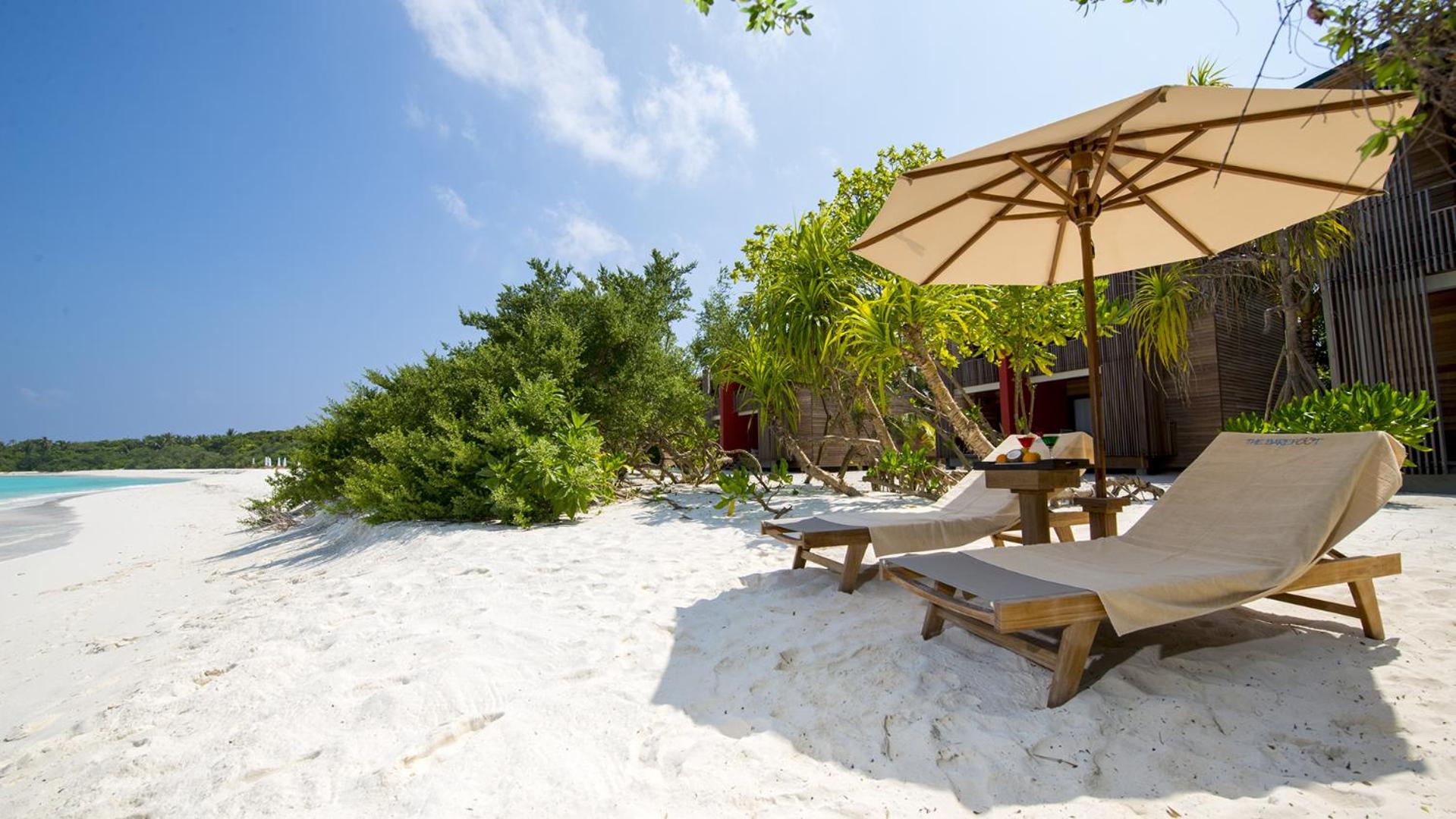 Sauļošanās krēsli un saulessargs The Barefoot Eco Hotel pludmalē ar skatu uz plašo okeāna krasta līniju un tropu apstādījumiem