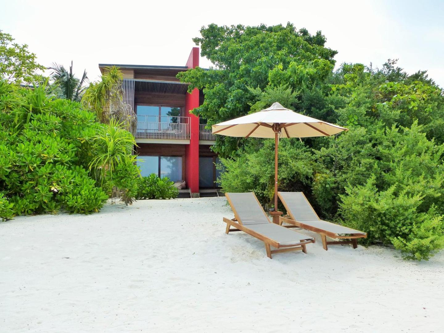 The Barefoot Eco Hotel divstāvu koka korpuss ar balkoniem un sauļošanās krēsliem baltu smilšu pludmalē starp zaļojošiem tropu augiem
