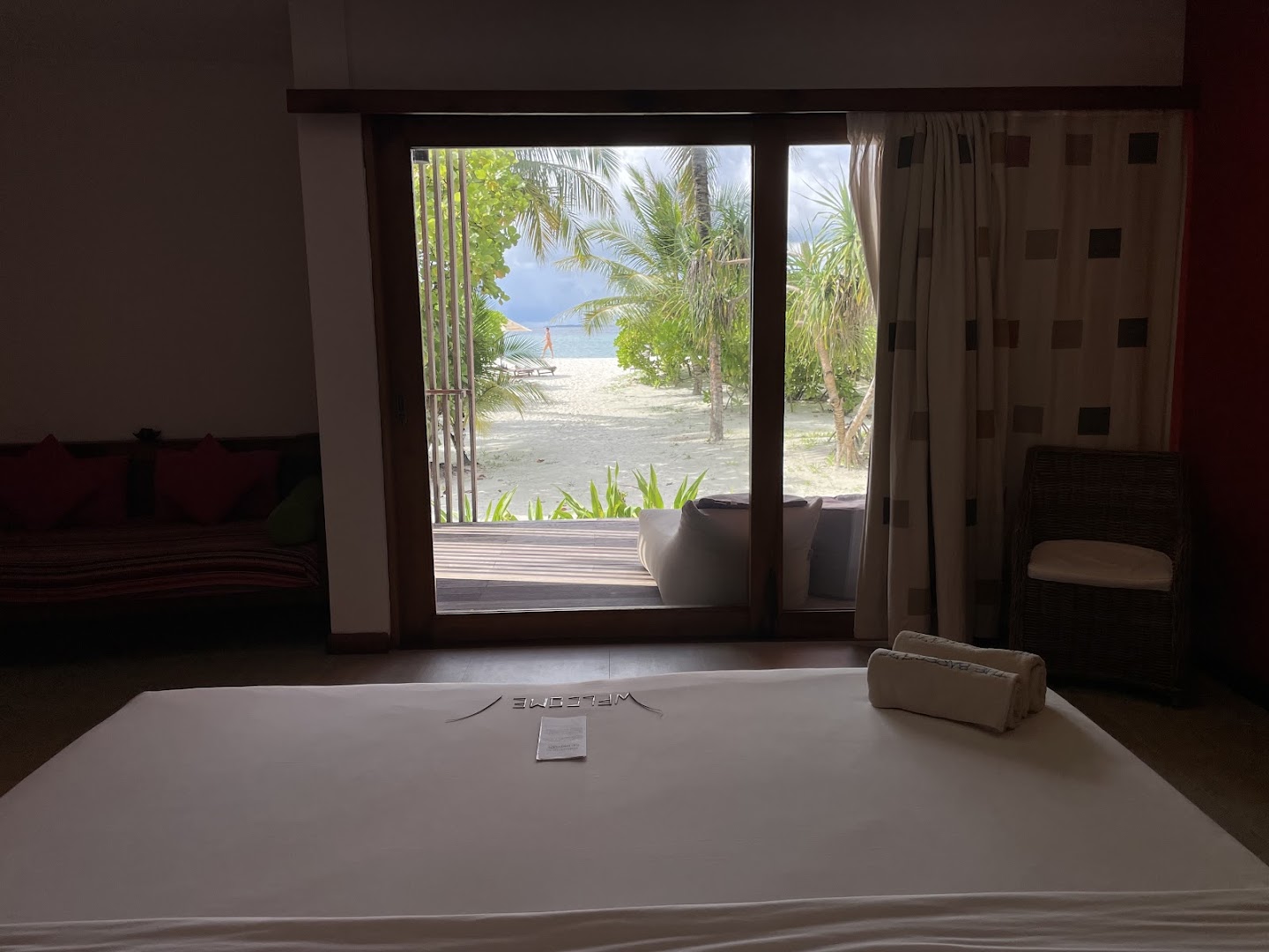 Skats no The Barefoot Eco Hotel gultas caur stikla durvīm uz Maldīvu pludmali un palmām