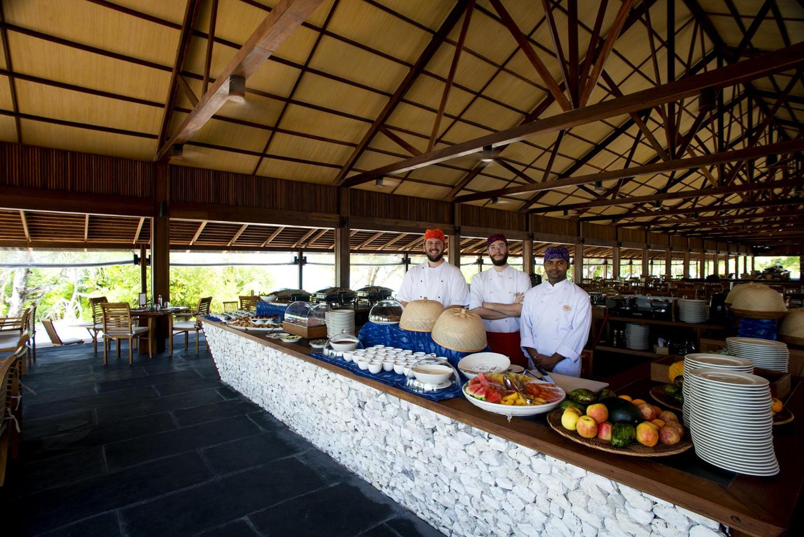 The Barefoot Eco Hotel restorāna darbinieki pie bufetes galda ar augļiem un uzkodām zem augstiem koka griestiem