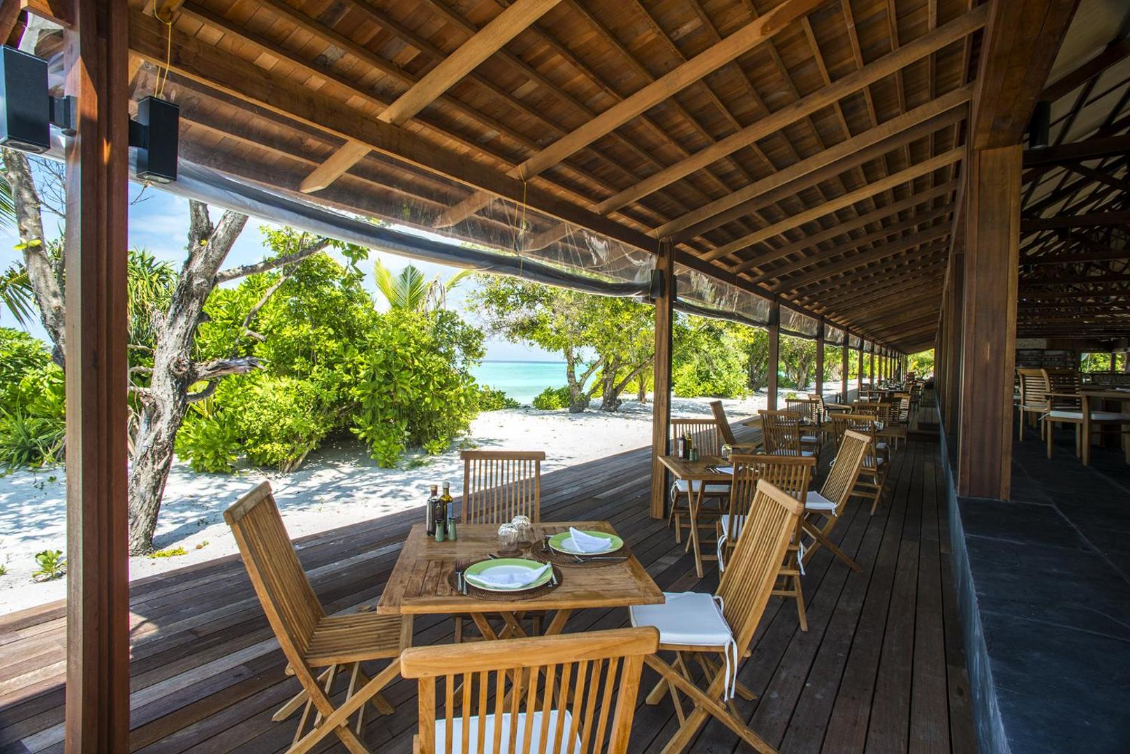 The Barefoot Eco Hotel restorāna āra terase ar koka mēbelēm un skatu uz pludmali un zaļajiem augiem