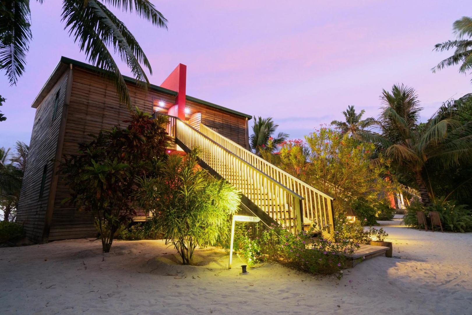 The Barefoot Eco Hotel divstāvu koka numuri ar izgaismotām kāpnēm un tropu dārzu saulrieta laikā Maldivu salās