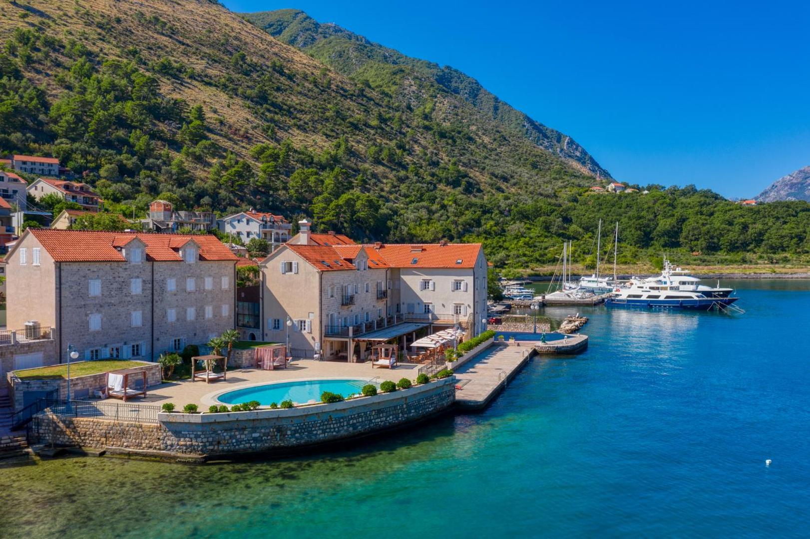 Panorāmas skats uz viesnīcu Splendido, baseinu un Kotoras līča zilo ūdeni uz stāvu, zaļu kalnu fona Melnkalnē