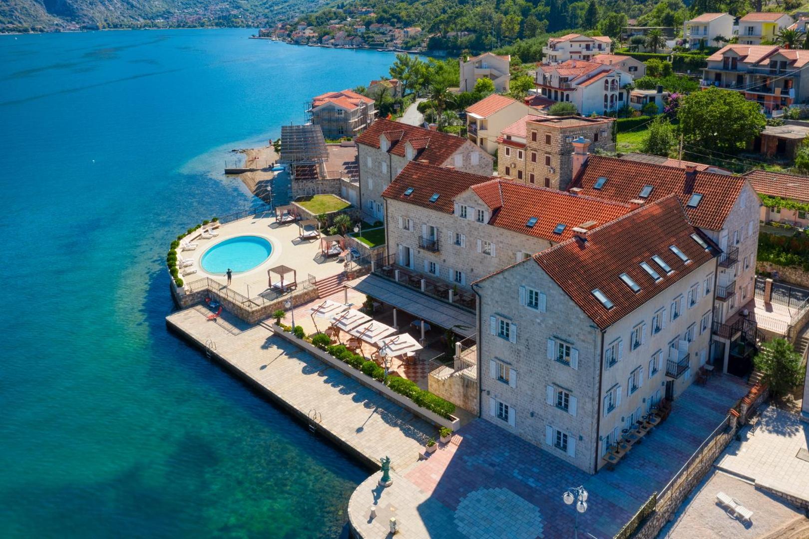 Viesnīcas Splendido skats no augšas uz āra baseinu un akmens ēkām Kotoras līča piekrastē, Melnkalnē ar saulessargiem un atpūtas krēsliem