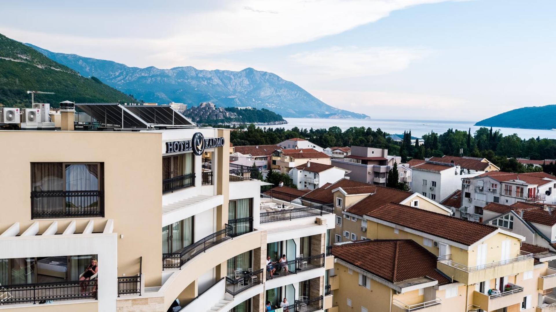 Hotel Kadmo by Aycon skats no augšas uz Budvas pilsētu un Adrijas jūru Melnkalnē ar kalniem fonā un viesnīcas balkoniem