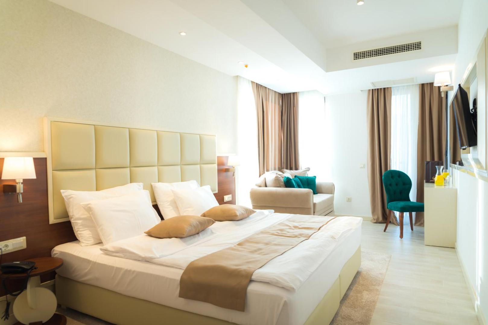 Hotel Kadmo by Aycon gaišs un mūsdienīgs viesnīcas numurs Budvā, Melnkalnē — liela gulta, atpūtas zona ar dīvānu un smalku interjeru