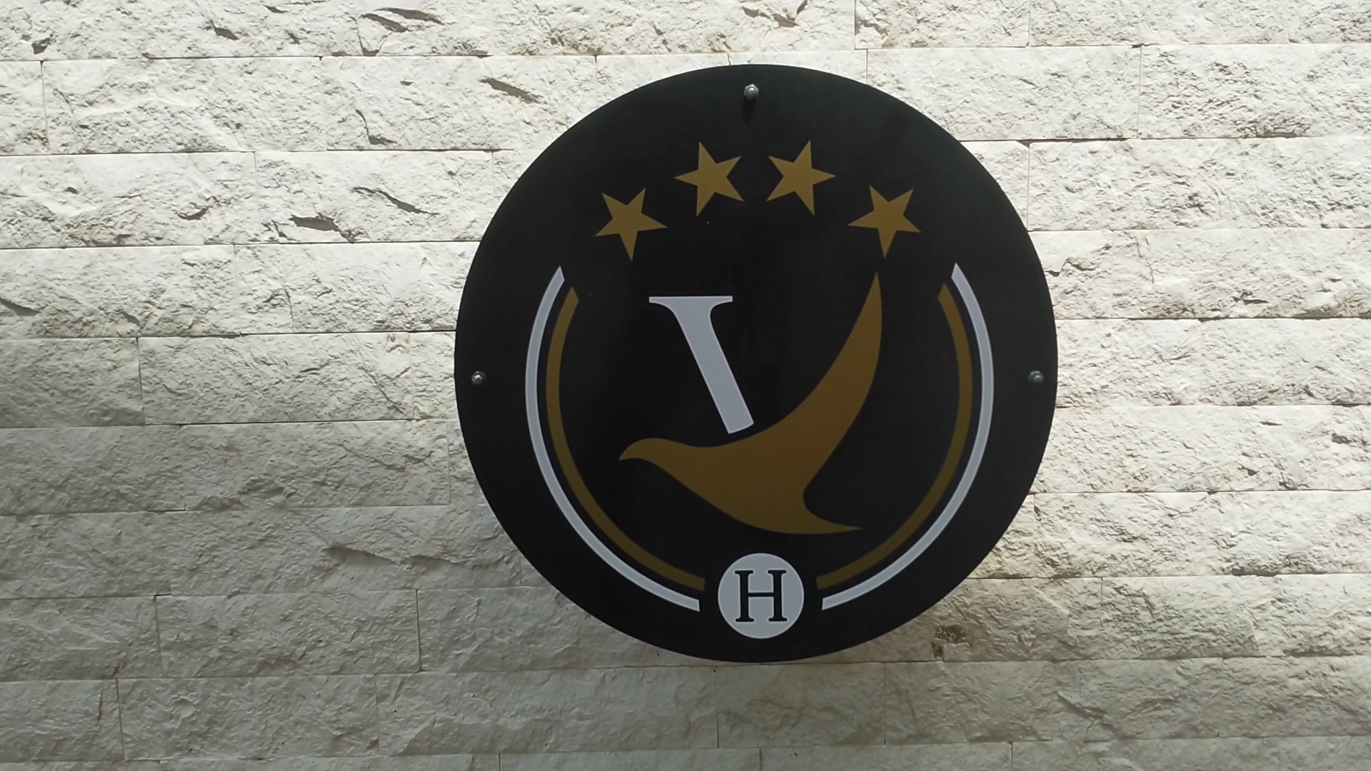 Kadmo by Aycon viesnīcas 4* logo uz akmens sienas Budvā, Melnkalnē — melns apaļš simbols ar zelta zvaigznēm